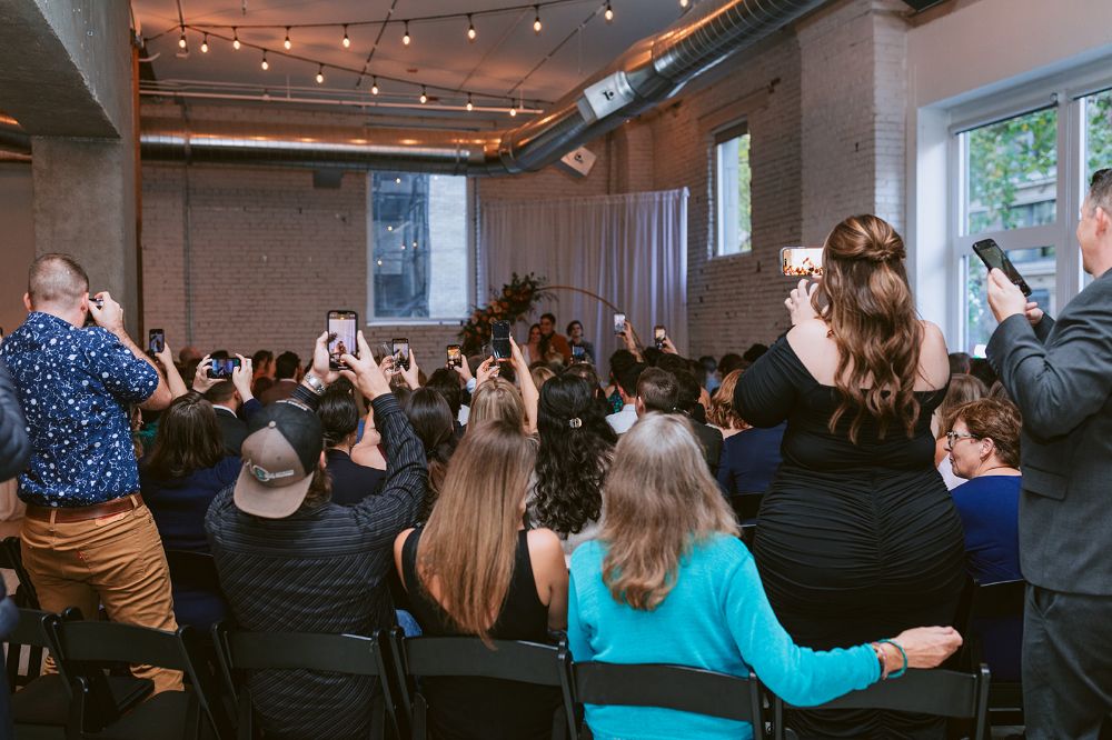 Wedding attendees use their smartphones to take photos of the happy newlyweds.