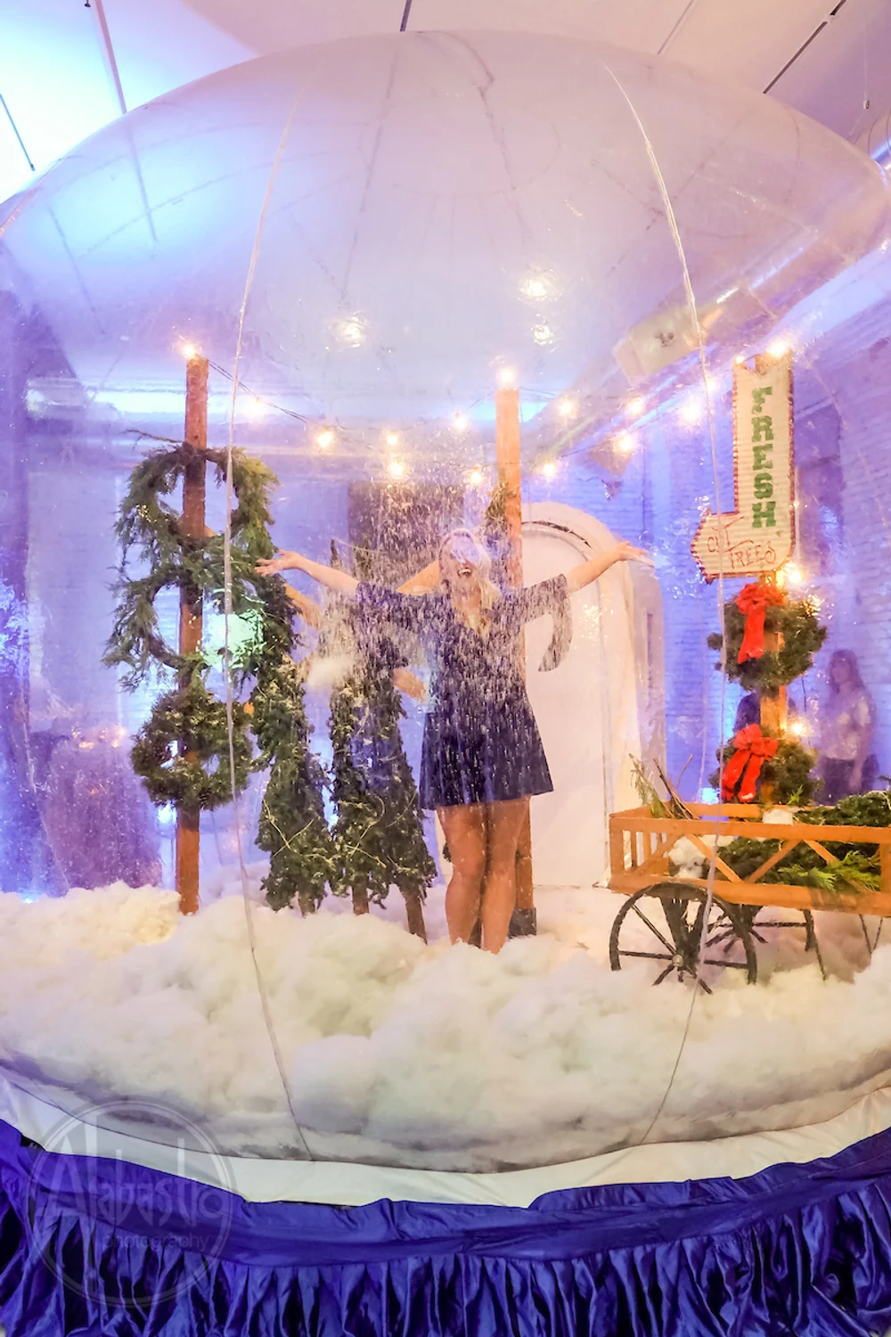 Woman standing inside of a giant snowglobe with holiday decorations and fake snow at a holiday office party, at THE 101 in Seattle, WA.