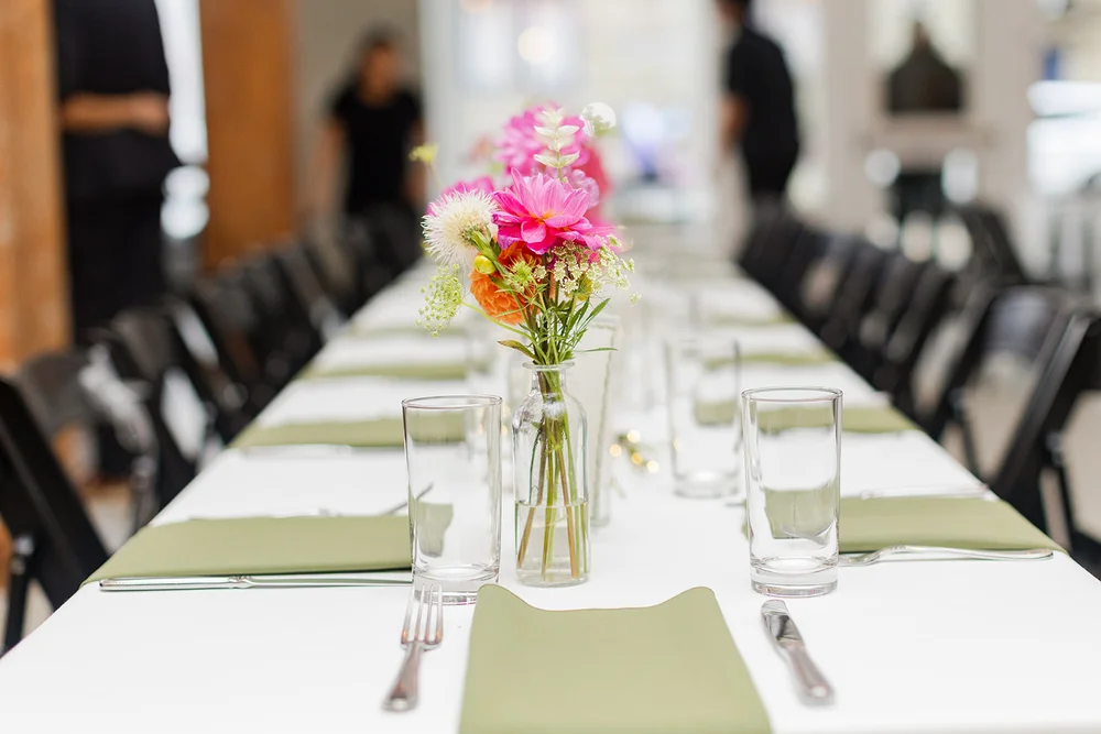 Reception tablescape with white linens, green napkins, and pink floral centerpieces.